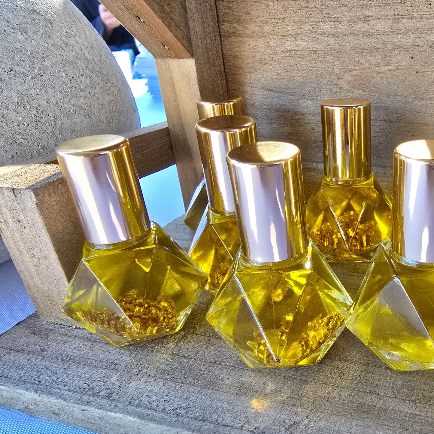 Collection of glass roller ball bottles filled with golden Nativity oil with gold flakes and gold caps on a rustic wood stable