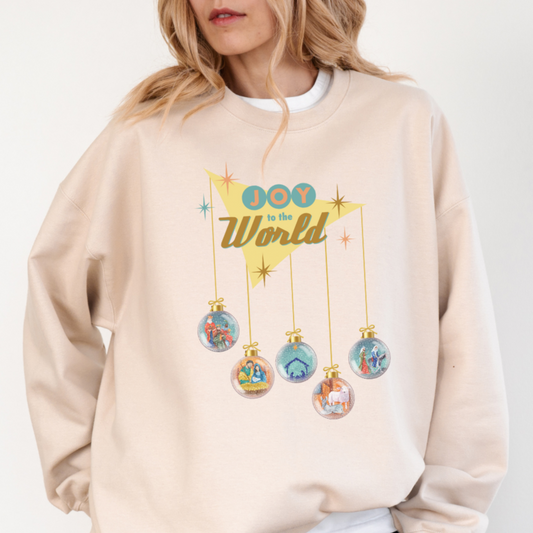 Woman wearing ivory Joy to the World Christmas sweater with retro design. Five ornaments hang down to depict the Nativity scene. 