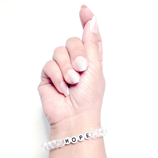 Close-up of a wrist wearing a bracelet showing clear pony beads and round white beads with black lettering that spells HOPE"