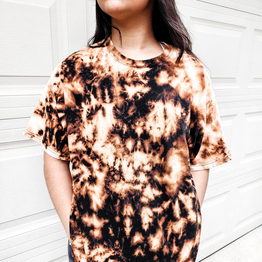 Woman wearing Refined by Fire bleached tee with unique black and tan tie-dye pattern against white garage door.