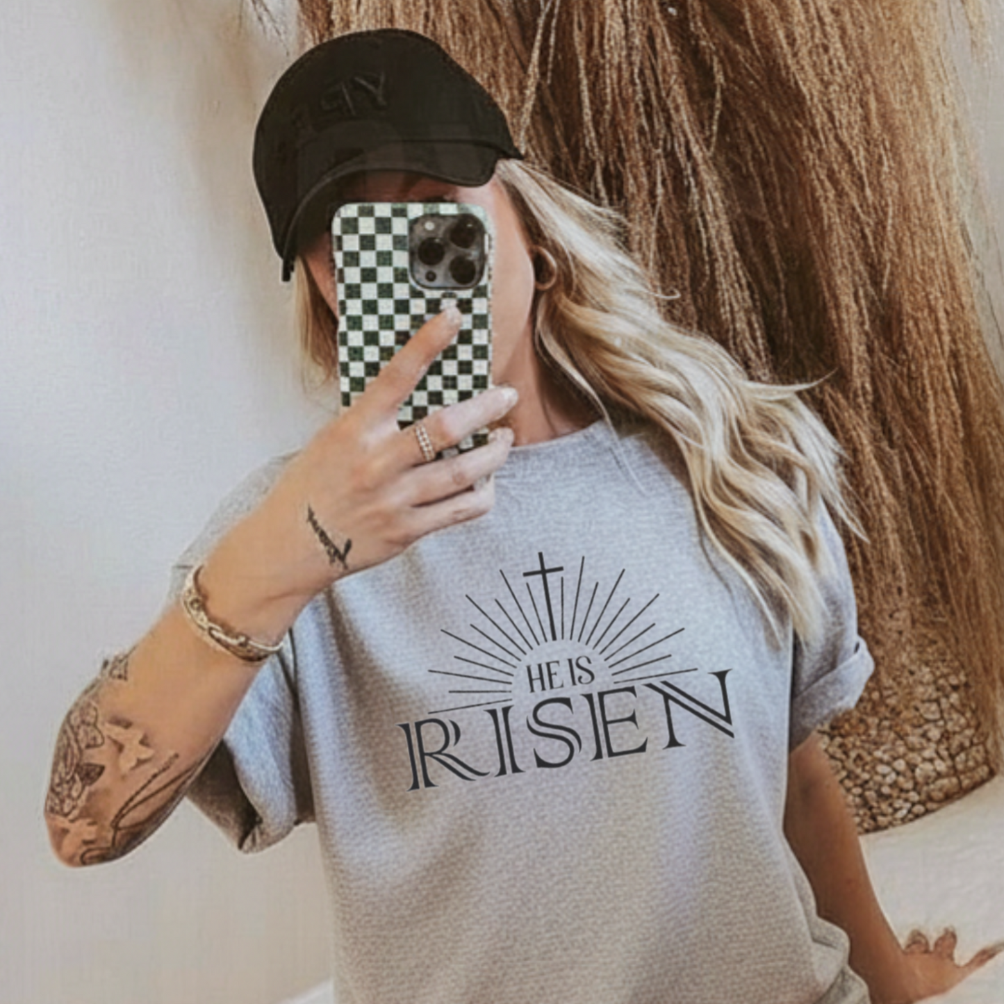 Person wearing a sports gray t-shirt with 'He is Risen' text, taking a mirror selfie.
