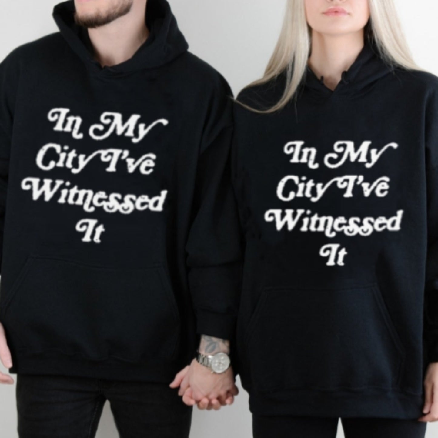 Couple wearing black I've Witnessed It Christian hoodies with white text design, front view