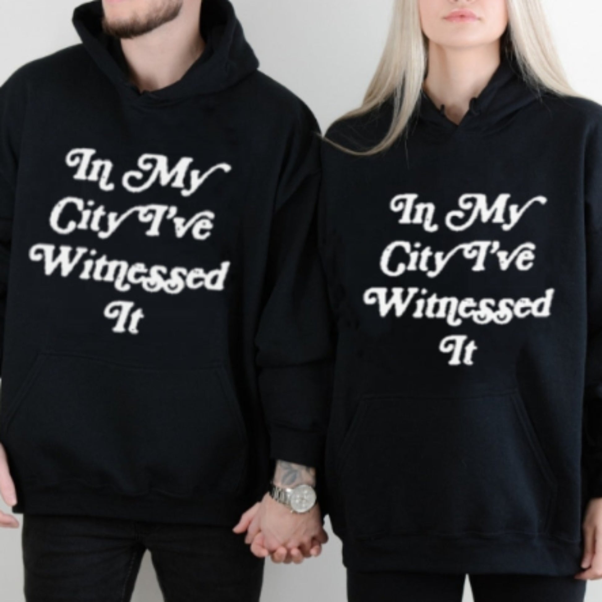 Couple wearing black I've Witnessed It Christian hoodies with white text design, front view