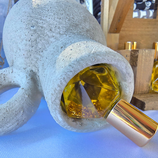 Bethlehem anointing oil blend in a roller ball glass bottle with gold flakes inside, with gold cap displayed in a white clay vase
