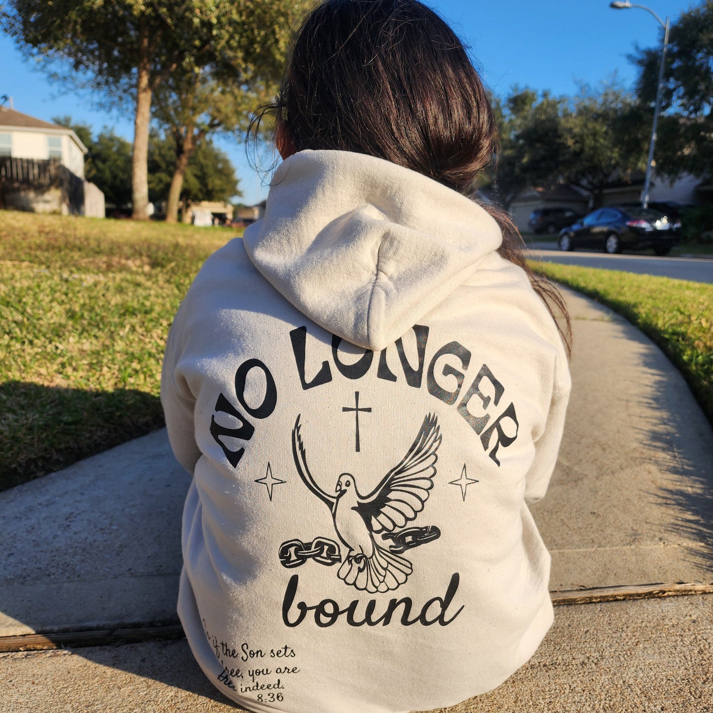 Teen wearing an ivory graphic hoodie with No Longer Bound text outdoors