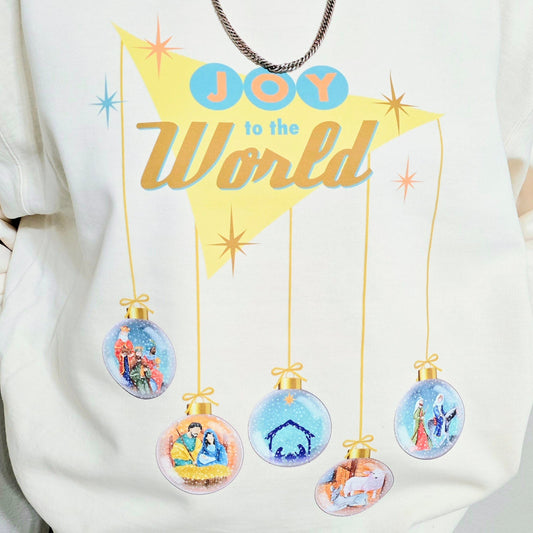 Closeup of a woman wearing  an ivory Joy to the World Christmas sweater with retro design. Five ornaments hang down to depict the Nativity scene. 