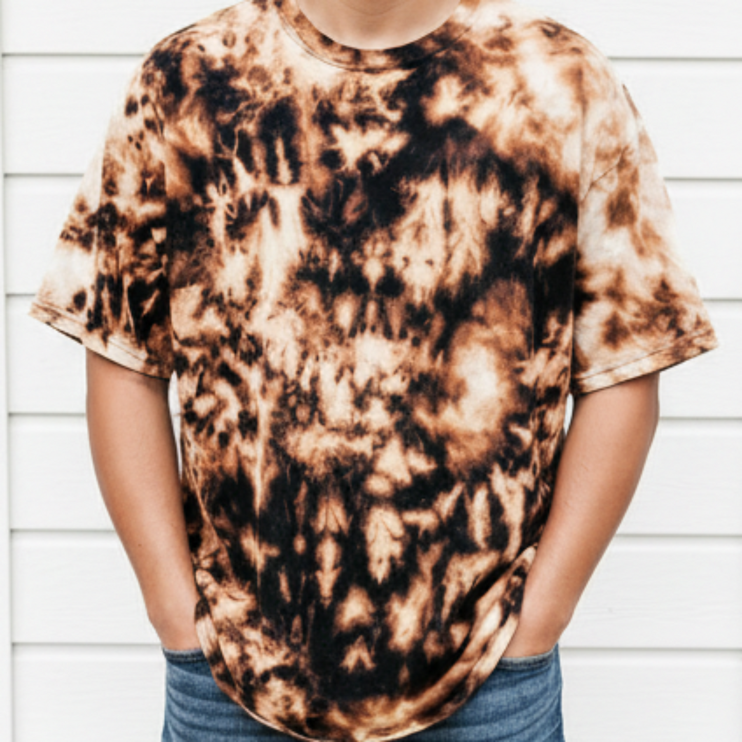 Man wearing Refined by Fire bleached tee with unique black and tan tie-dye pattern styled with jeans against white background